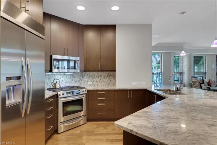 Kitchen featuring stainless steel appliances, light stone countertops, light wood-style floors, hanging light fixtures, and a peninsula