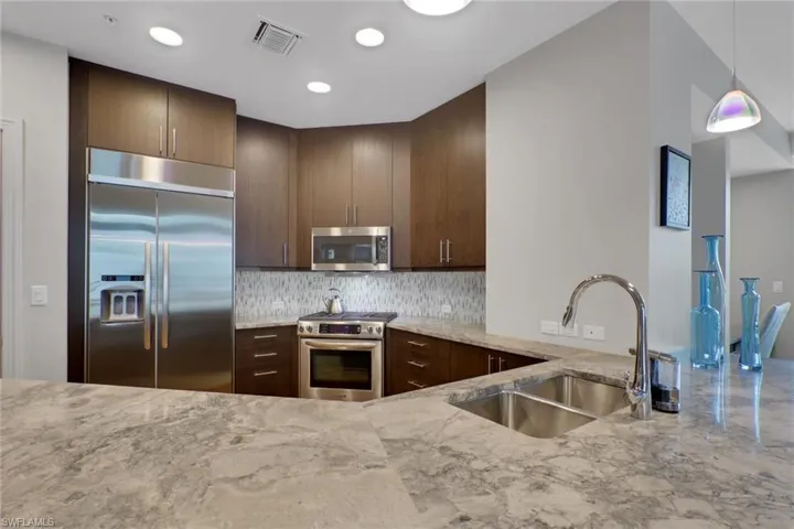 Kitchen featuring stainless steel appliances, light stone countertops, tasteful backsplash, dark wood finish cabinets, and pendant lighting