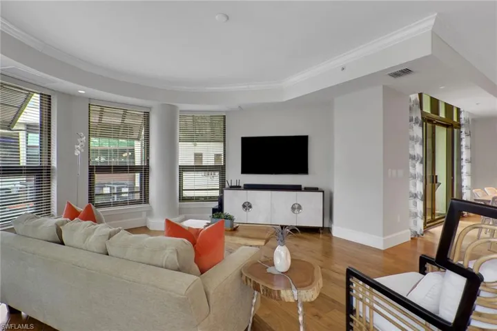 Living area with ornamental molding, wood finished floors, and a raised ceiling