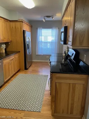 Kitchen with wood finish cabinetry, dark stone countertops, refrigerator, a textured ceiling, and light wood-style flooring
