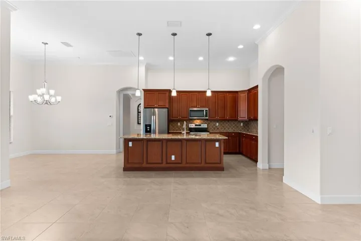 Kitchen with arched walkways, pendant lighting, appliances with stainless steel finishes, a kitchen island with wood wrap veneer