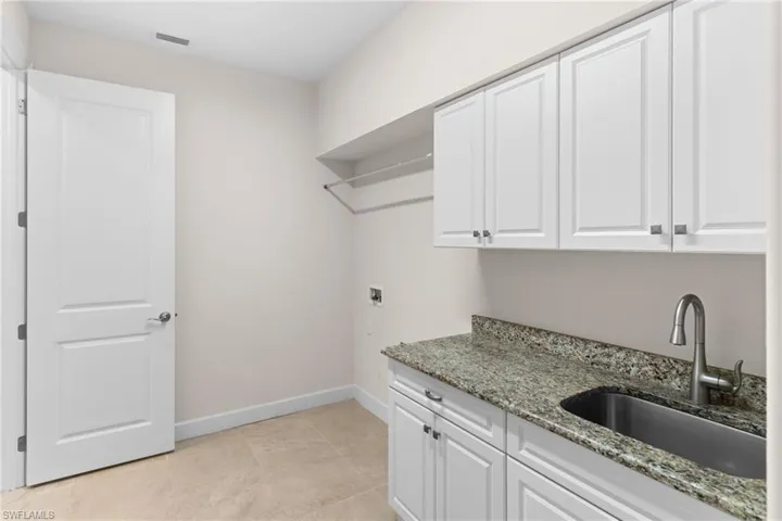 Laundry room includes cabinets, and light tile patterned floors, with stainless steel sink