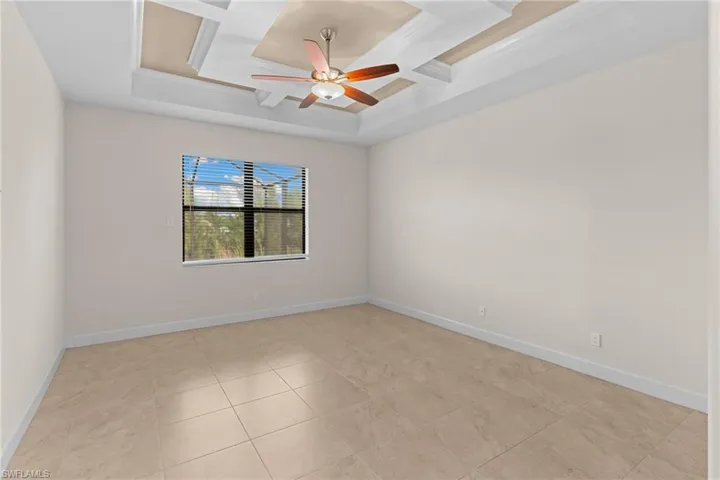 Tastefully designed primary bedroom, ceiling fan, coffered ceiling, light tile patterned floors, and ornamental molding