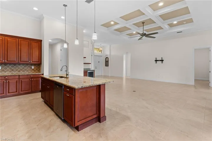 Kitchen with arched walkways, coffered ceiling, an island with sink, crown molding, and recessed lighting