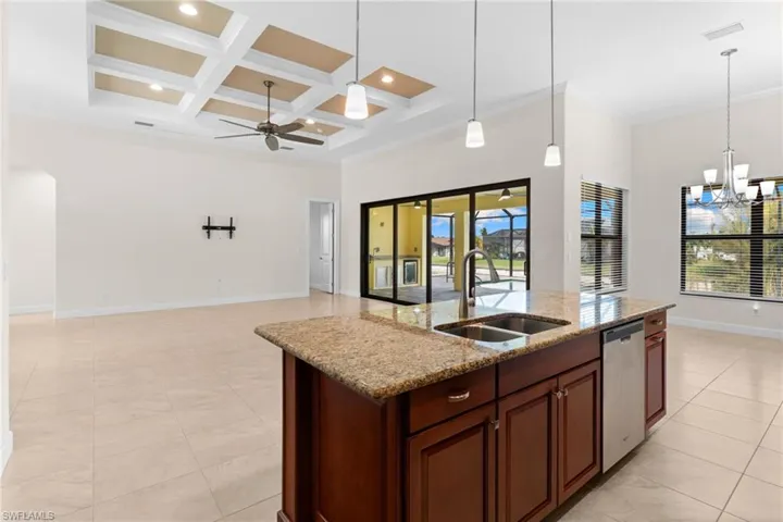 Kitchen with hanging light fixtures, coffered ceiling, a chandelier, light stone counters, and crown molding