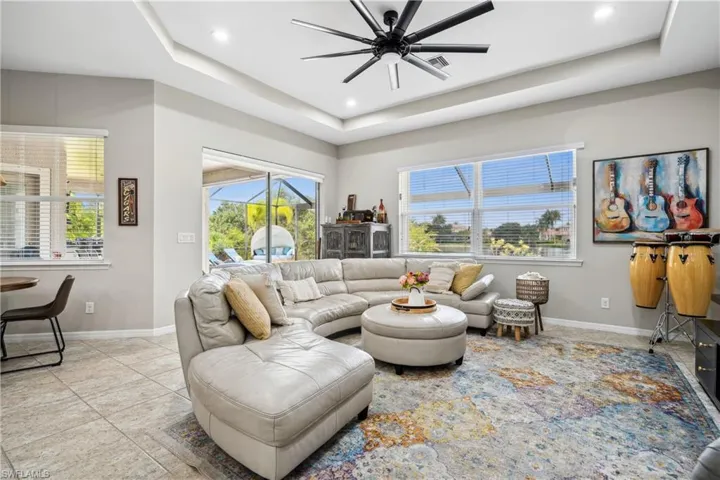 Living room with a tray ceiling, light tile patterned floors, and ceiling fan