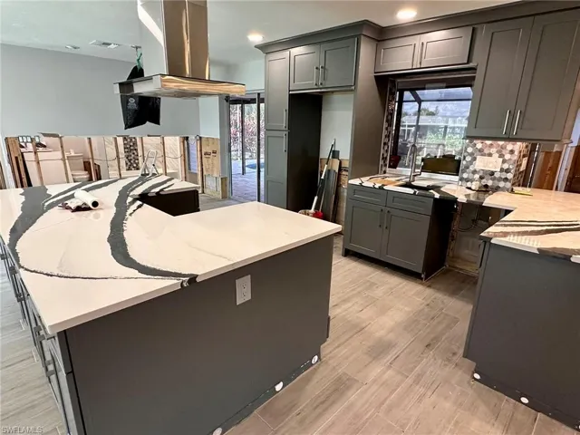 Kitchen featuring gray cabinets, island range hood, a center island, light hardwood / wood-style floors, and light stone countertops