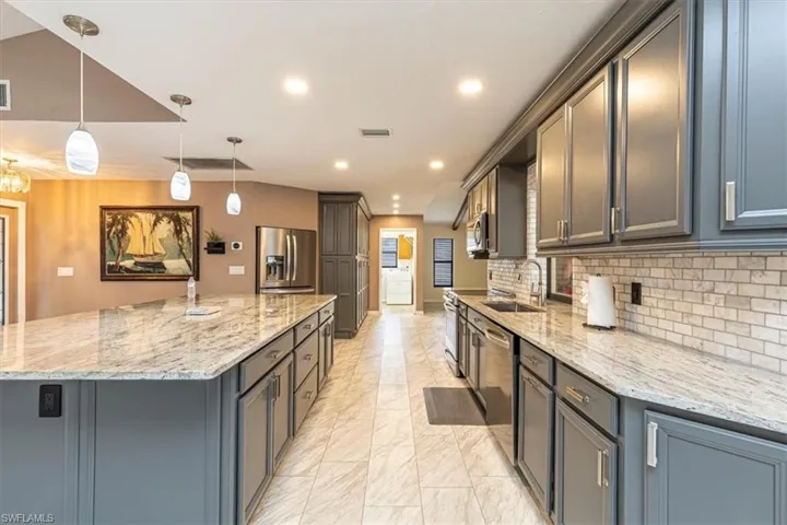 Kitchen featuring hanging light fixtures, light stone counters, appliances with stainless steel finishes, light marble finish floors, and a large island