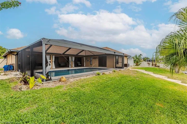 Back of property featuring a sunroom, glass enclosure, an outdoor pool, a lawn, and a patio area