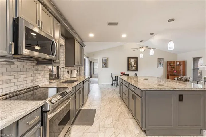 Kitchen featuring a ceiling fan, appliances with stainless steel finishes, pendant lighting, light stone countertops, and vaulted ceiling