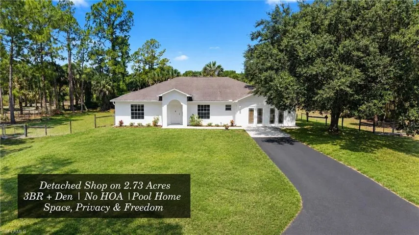 White stucco residence with a paved driveway, front lawn, and mature trees