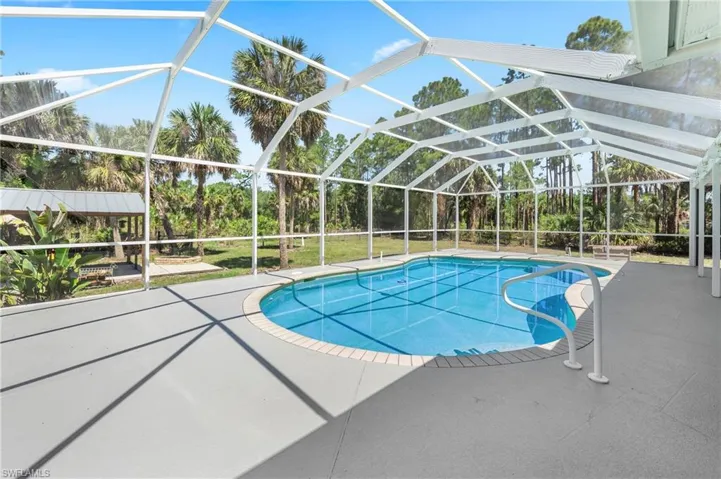 Screen-enclosed pool area featuring a blue-tiled swimming pool, a light grey concrete deck, and a white pool handrail
