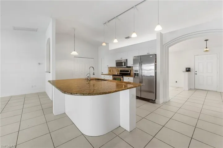 Kitchen featuring a large island with a stone countertop and integrated sink, stainless steel appliances, white cabinetry, and tile flooring