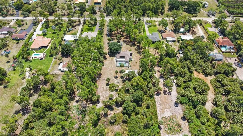 Aerial view showcasing a residential property with a central home, an in-ground swimming pool, and extensive surrounding green space with mature trees