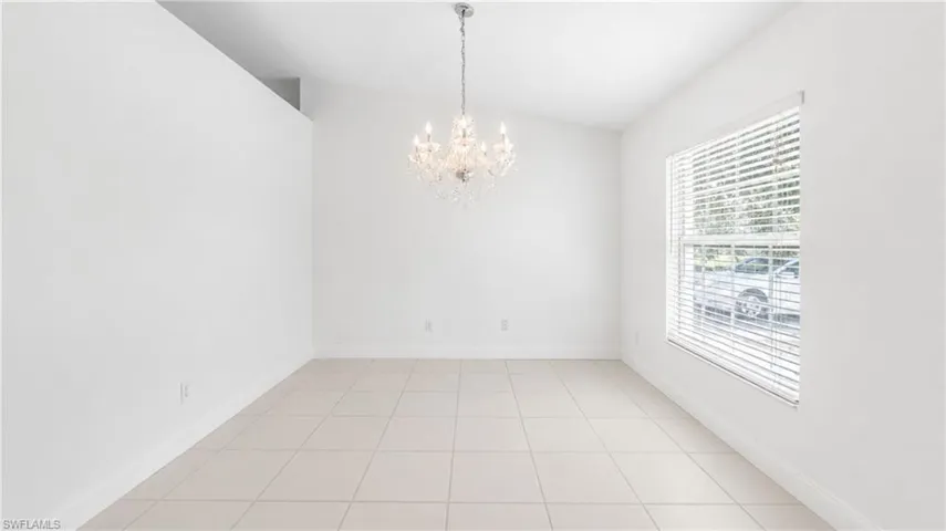 Spacious room with white walls, tiled flooring, and a decorative chandelier