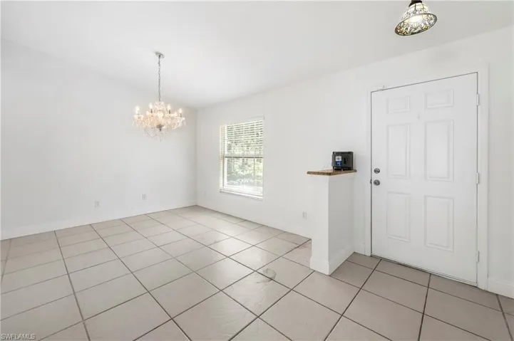 Spacious room featuring neutral tile flooring, a large window with horizontal blinds, and a decorative crystal chandelier