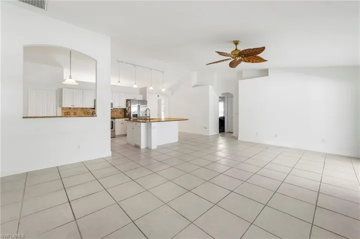 Open-concept living space featuring neutral tile flooring, a kitchen with white cabinetry and a breakfast bar, stainless steel appliances, and a tropical-inspired ceiling fan