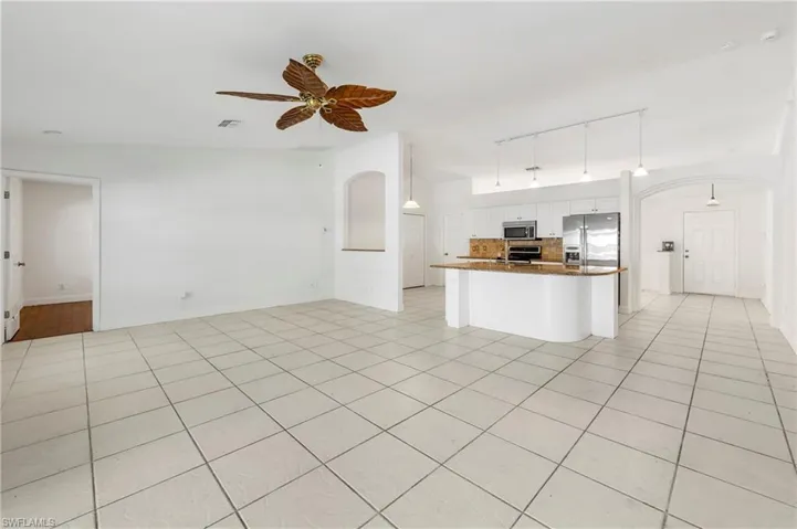 Open-concept living area featuring light-colored tile flooring, white walls, and a decorative ceiling fan