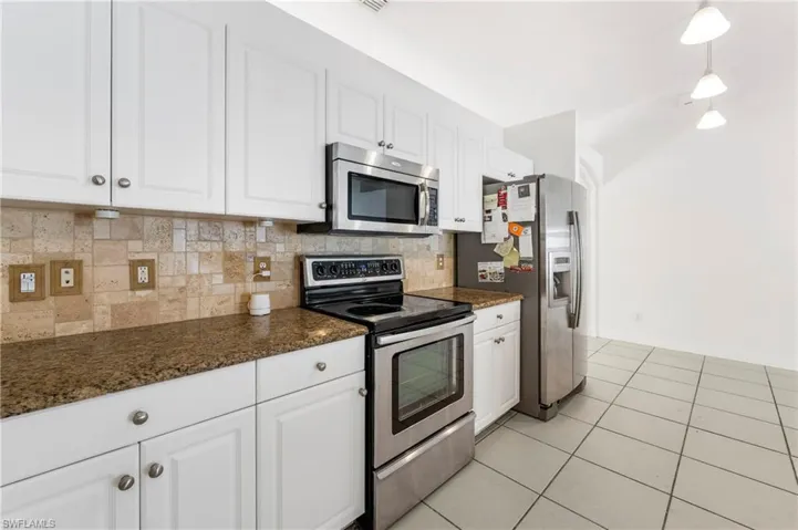 Kitchen featuring white cabinetry with silver hardware, speckled stone countertops, and a tiled backsplash