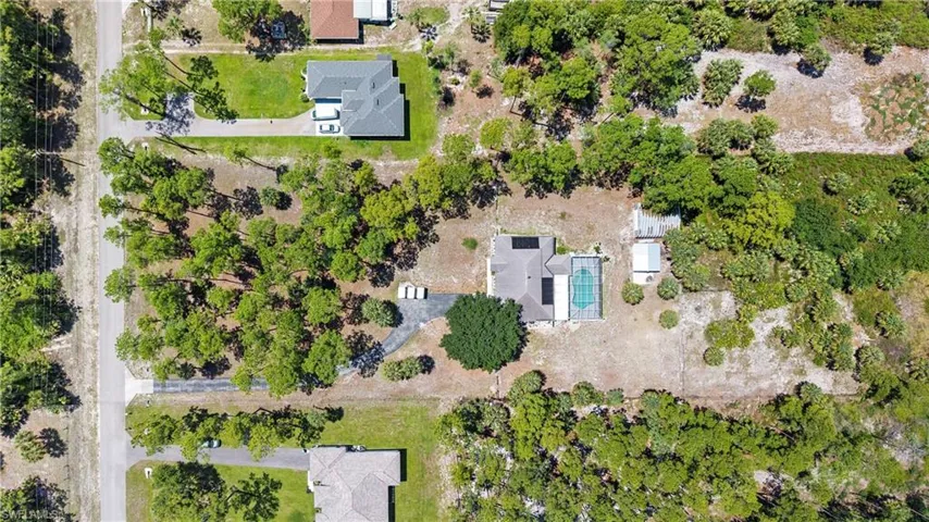 Aerial view showcasing a residential property with a private pool, an adjacent outbuilding, and mature trees on the lot