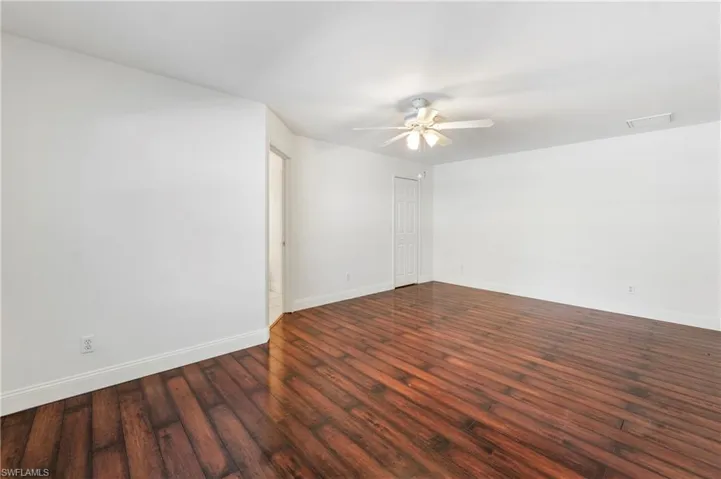 Spacious interior room featuring rich wood-finish flooring, crisp white walls, a ceiling fan with integrated lighting, and white baseboards