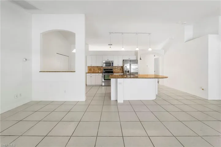 Kitchen featuring a curved island with stone countertop, stainless steel appliances, white cabinetry, and pendant lighting