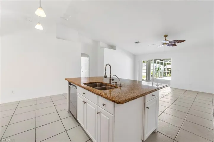 Kitchen island with a double basin sink, high-arc faucet, white cabinetry, and granite-style countertop