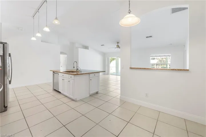 Open-concept kitchen featuring a center island with sink, white cabinetry, and granite countertops