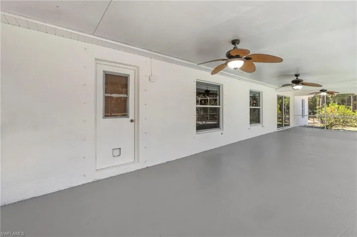 Expansive covered patio featuring a textured concrete floor, multiple ceiling fans with light kits, dual pane windows, and sliding glass doors