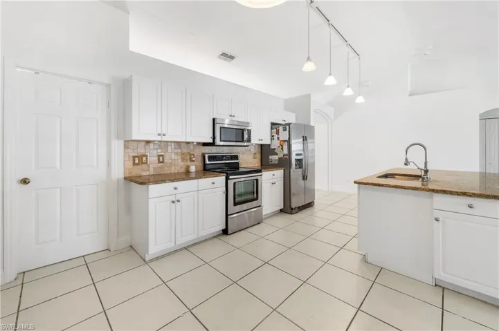 Kitchen featuring white cabinetry, stainless steel appliances, a tile backsplash, and a central island with a sink and stone countertop