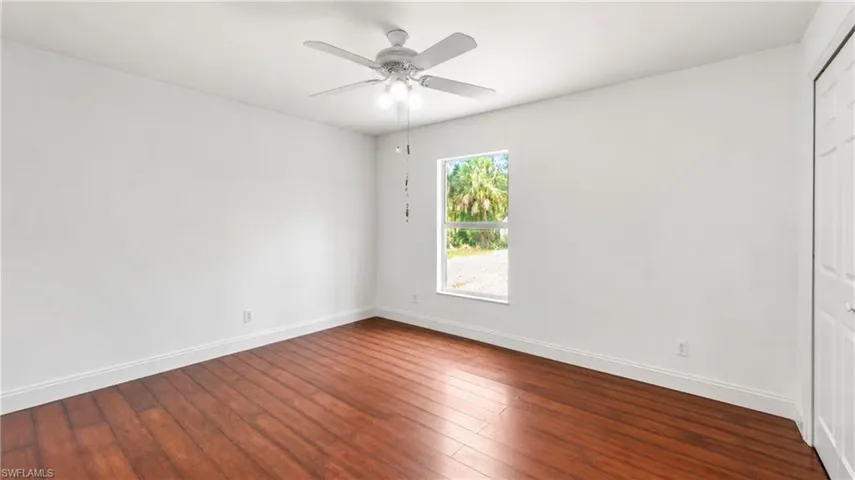 Bright interior space featuring rich wood-finish flooring, white baseboards, and a contemporary ceiling fan with integrated lighting