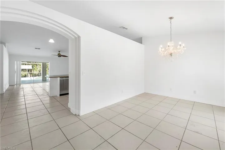 Spacious interior featuring neutral tile flooring, an elegant chandelier, and an arched entryway