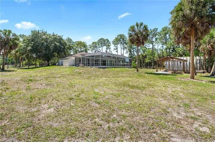 Expansive yard featuring a screened-in patio, mature palm trees, and an open-air pavilion