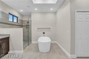 Bathroom featuring a freestanding tub, a shower stall, vanity, light wood-style flooring, and recessed lighting