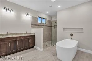 Bathroom featuring double vanity, a soaking tub, light wood finished floors, tiled shower, and recessed lighting