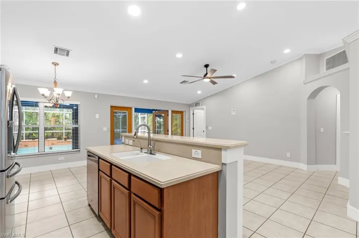 Kitchen featuring wood finish cabinets, a center island with sink, light countertops, hanging lights, and stainless steel appliances
