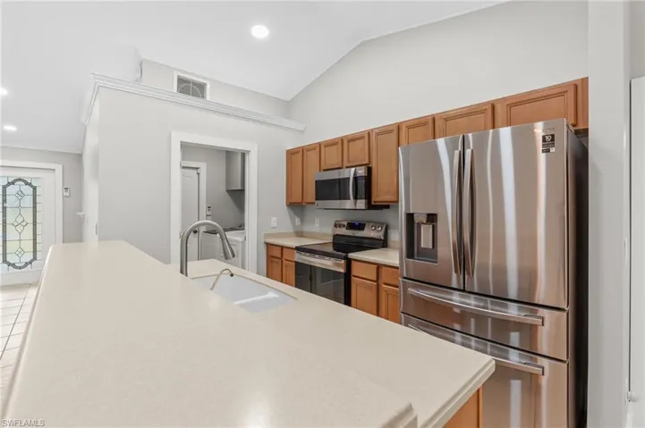 Kitchen with stainless steel appliances, recessed lighting, wood finish cabinetry, vaulted ceiling, and ornamental molding