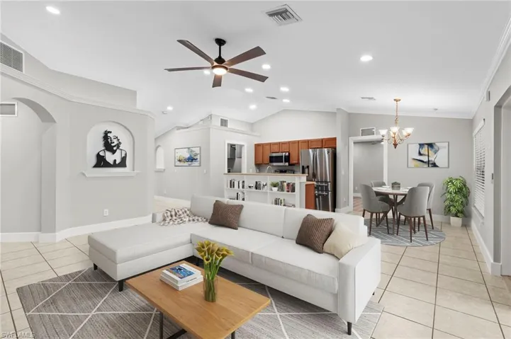 Living room with ceiling fan, hanging lights, light tile patterned flooring, lofted ceiling, and arched walkways