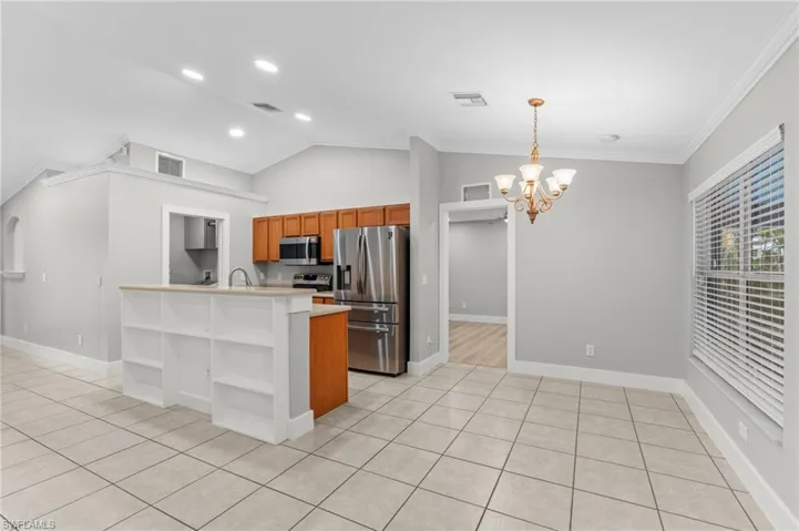 Kitchen featuring lofted ceiling, wood finish cabinetry, stainless steel appliances, a chandelier, and light tile patterned flooring