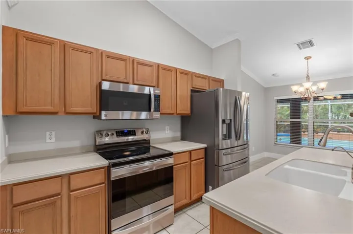 Kitchen with stainless steel appliances, light tile patterned floors, hanging lights, lofted ceiling, and ornamental molding