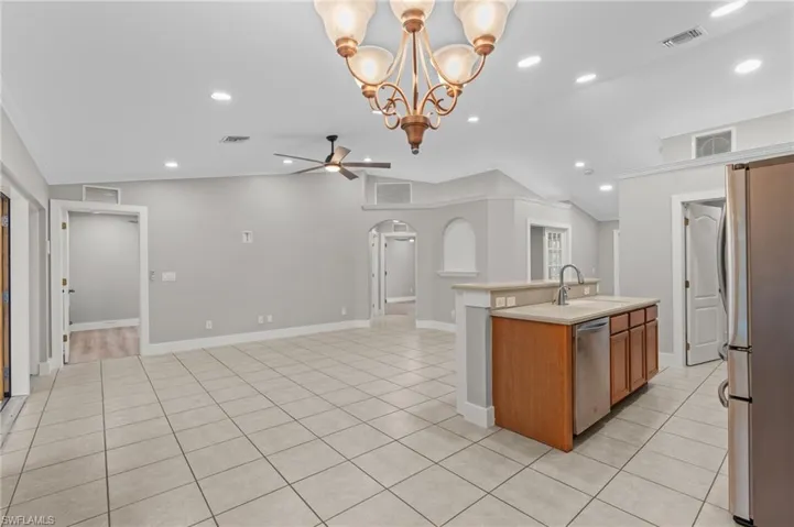 Kitchen with arched walkways, a chandelier, a center island with sink, stainless steel appliances, and wood finish cabinets