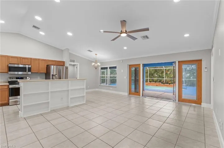 Unfurnished living room featuring ceiling fan, vaulted ceiling, hanging lights, light tile patterned floors, and crown molding