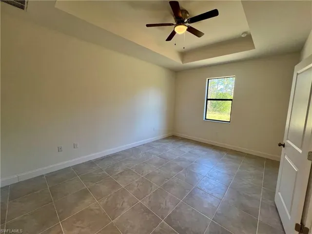 Primary bedroom with tray ceiling and tile floors.