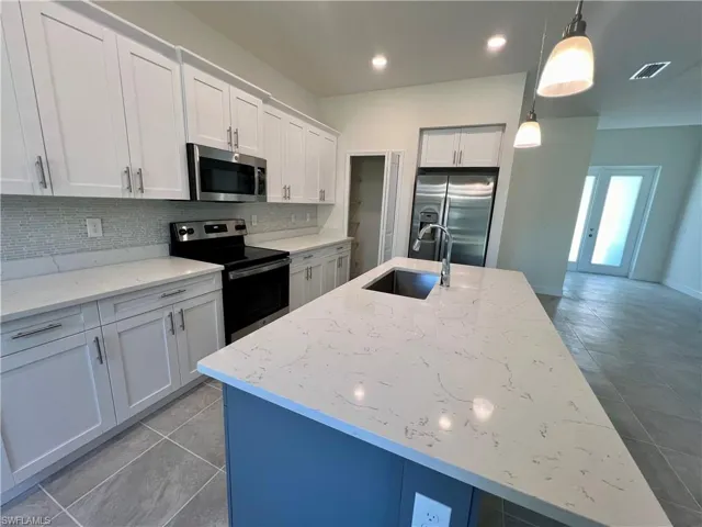 Kitchen featuring white cabinetry, sink, decorative light fixtures, a center island with sink, and appliances with stainless steel finishes with QUARTZ TOPS.