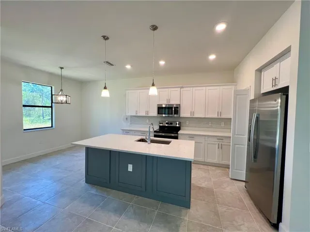Kitchen with white cabinetry, an island with sink, decorative light fixtures, and appliances with stainless steel finishes with QUARTZ TOPS.