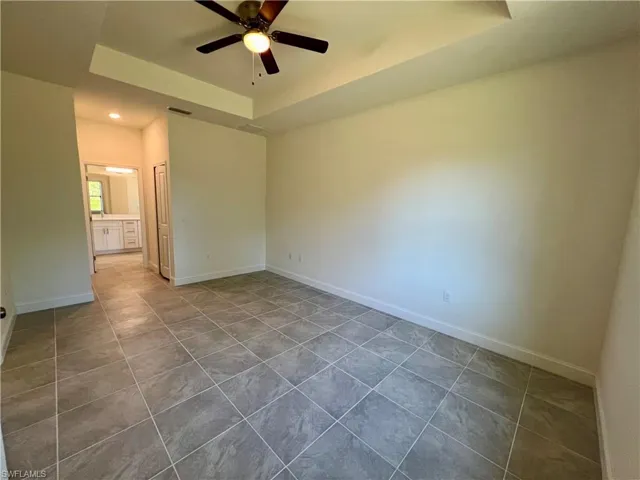 Primary bedroom with tray ceiling and tile floor and walk in closet.