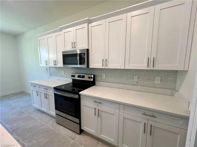 Kitchen with glass tile backsplash, white cabinets, light tile patterned flooring, QUARTZ counters, and stainless steel appliances