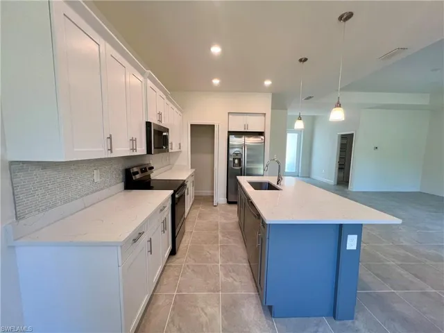 Kitchen with light QUART countertops, stainless steel appliances, white cabinetry, hanging light fixtures, and an island with sink