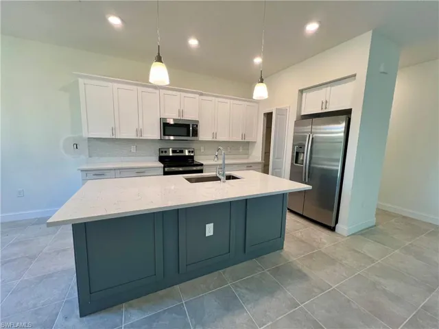 Kitchen with white cabinets, sink, hanging light fixtures, glass tile backsplash, and stainless steel appliances with QUARTZ TOPS.
