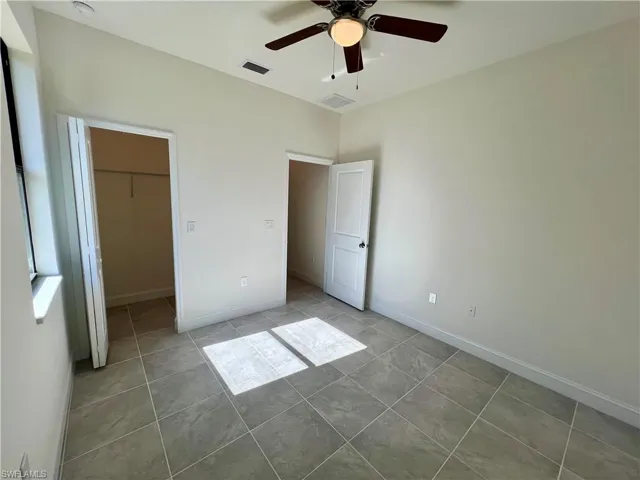 Guest bedroom featuring tile patterned floors, a spacious walk in closet, and ceiling fan